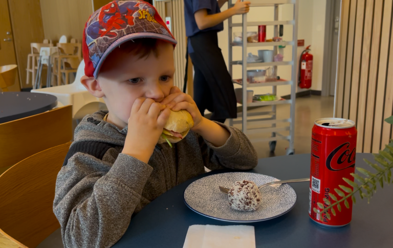 Ett barn sitter vid ett bord och äter dessert med en läsk bredvid.