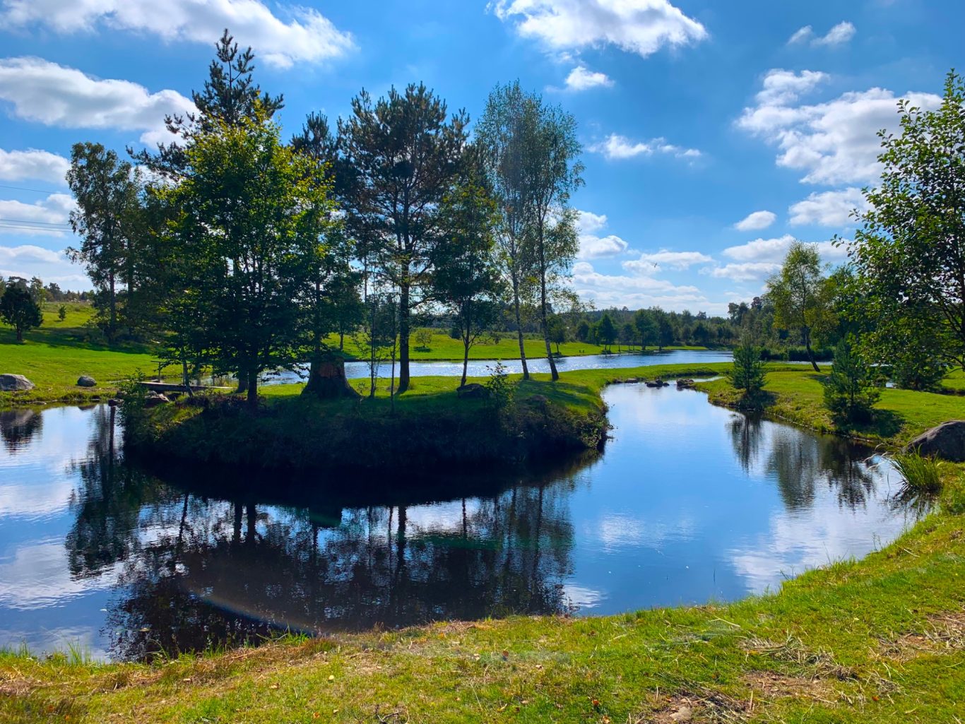 Flugströmmen i Sunnedamm Lugnt vattendrag med spegelblanka ytor och grönskande träd vid sidan.