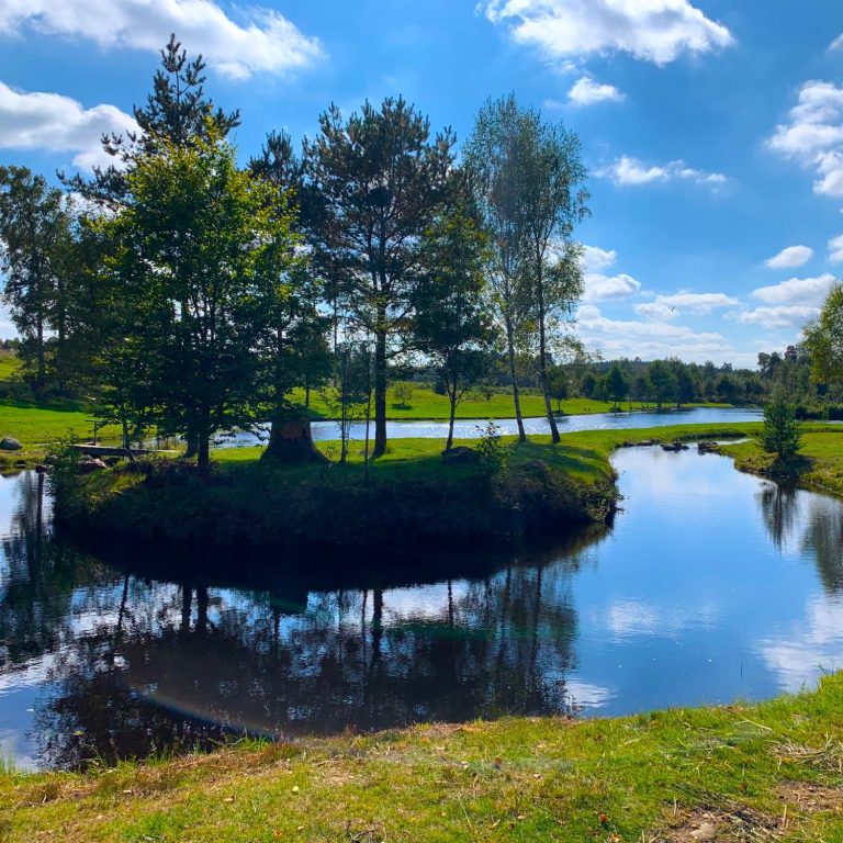 Lugn landskap med en spegelblanka sjö och trädkantade öar under en blå himmel.