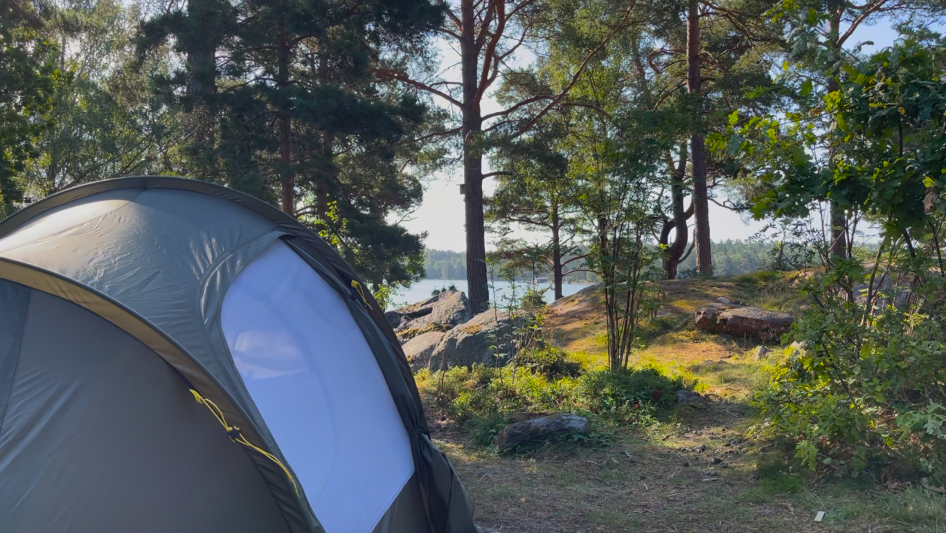 Havsutsikt från tältet Tält i naturlig miljö vid vattnet, omgiven av träd och stenar.