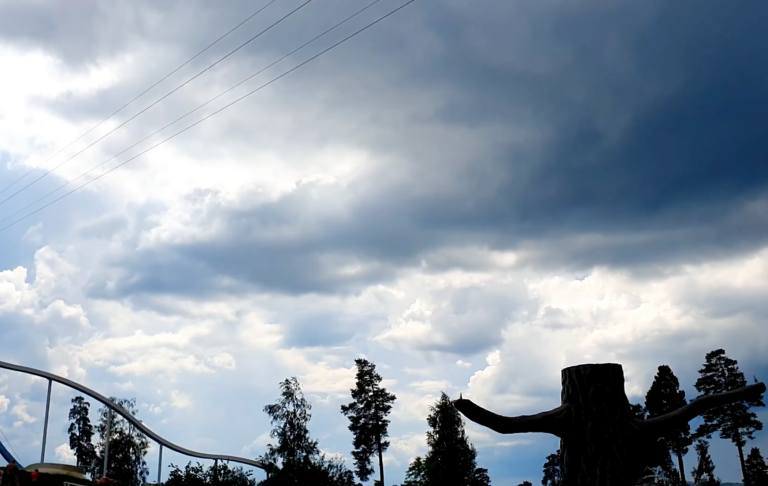 Mörka moln över en skog och en del av en berg- och dalbana.