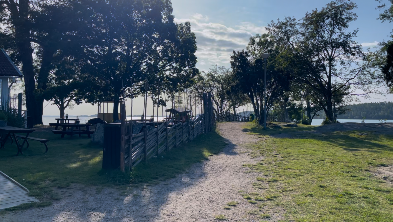 Väg till badbryggan Grusväg genom en park med träd och utsikt över en sjö.