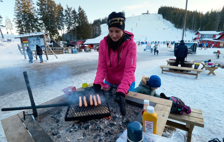 Kvinna grillar korv vid en utomhusplats i snöigt vinterlandskap.