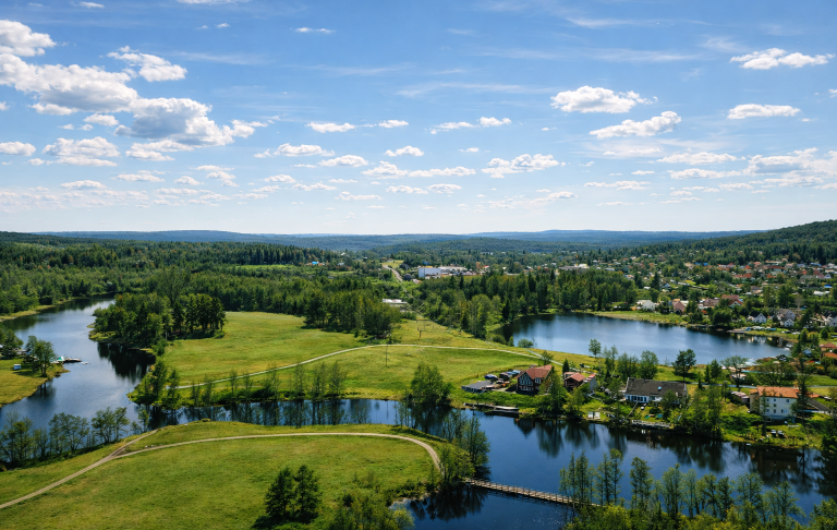 Lugn sjö med spegelblanka moln och grönska runt omkring.
