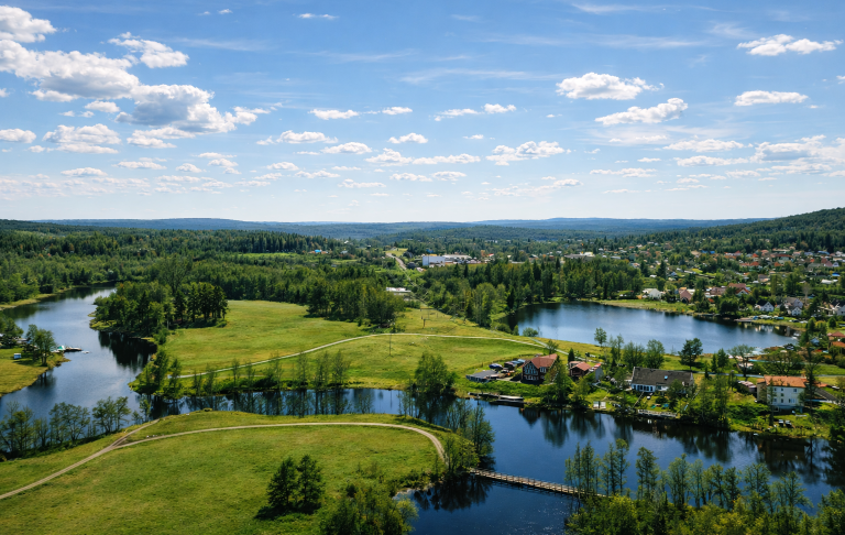 Landskap med floder, grönskande fält och små hus under en klarblå himmel.