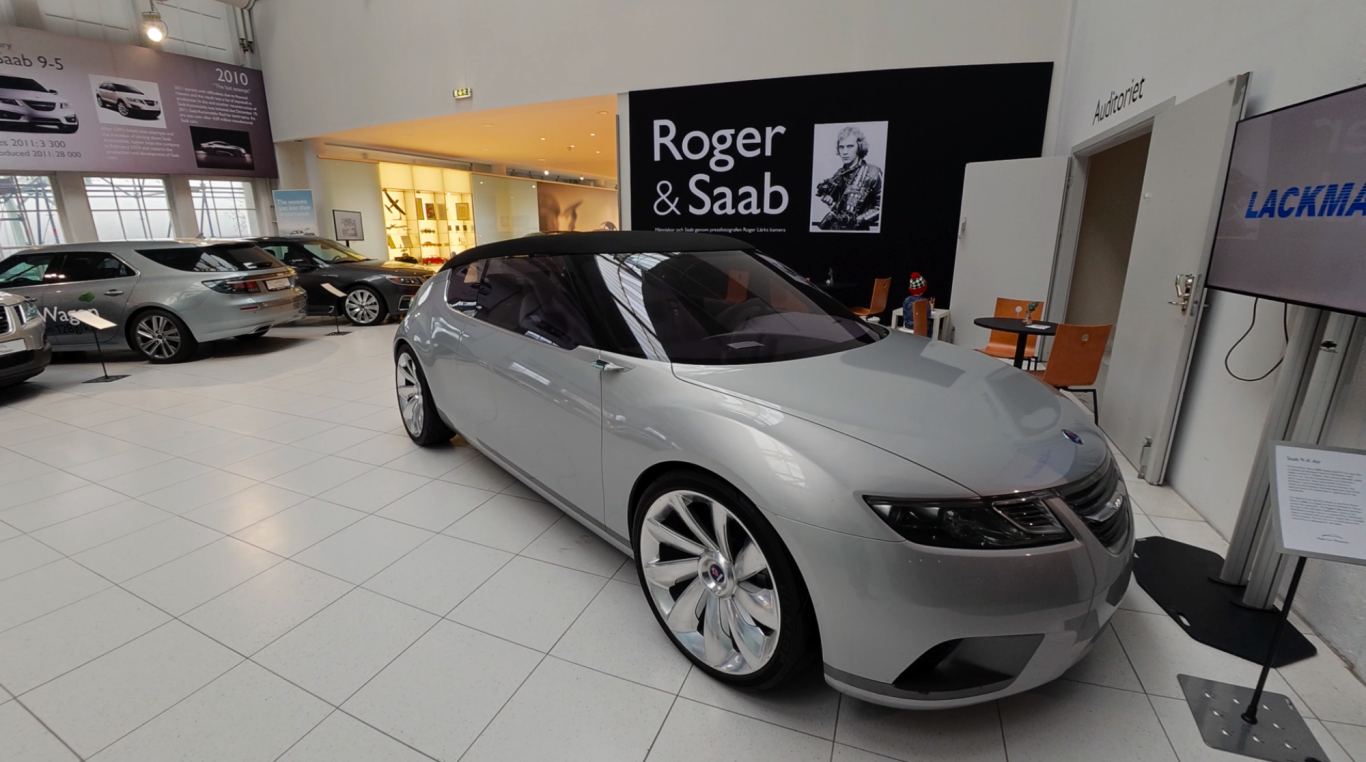 Saab Aero X Sölvfärgad bil i en modern bilutställning med ljusa väggar och annan bilar i bakgrunden.