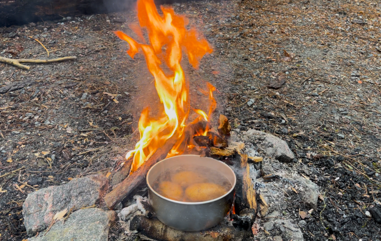 Eld brinner i en lägereld med en kastrull som kokar ovanpå.