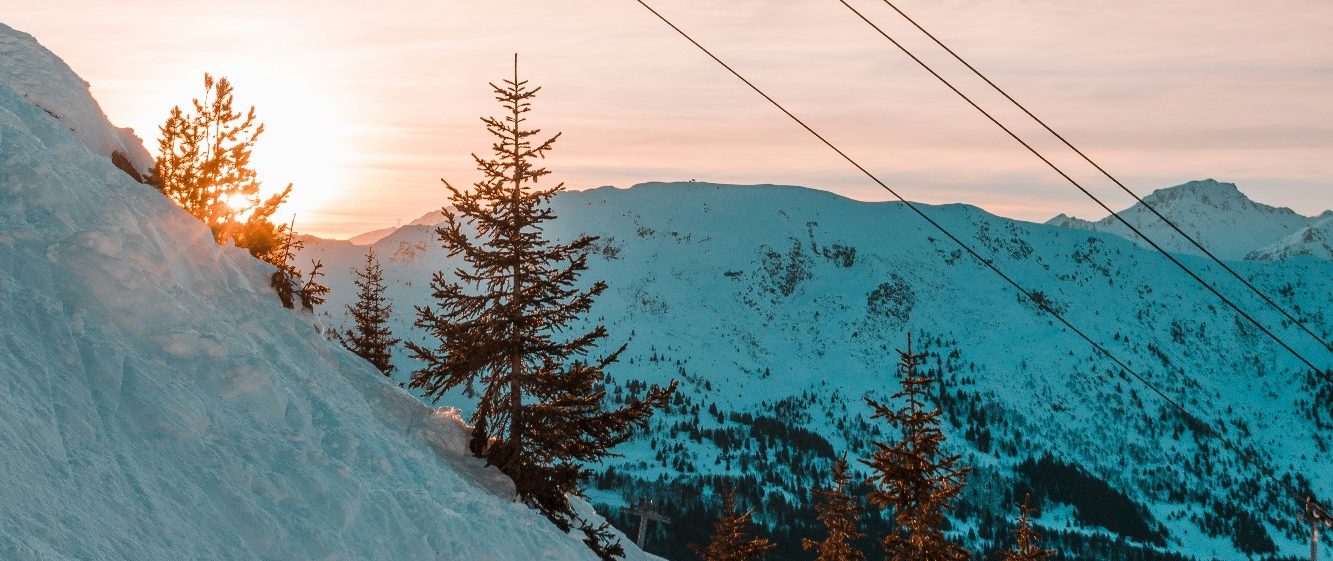 Solnedgång över snötäckta alpberg och träd i en vinterlandskap.