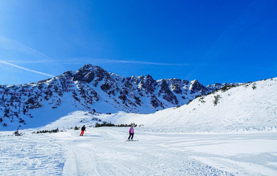 Pist med skidåkare i snöigt landskap och klara blå himmel i fjällen.