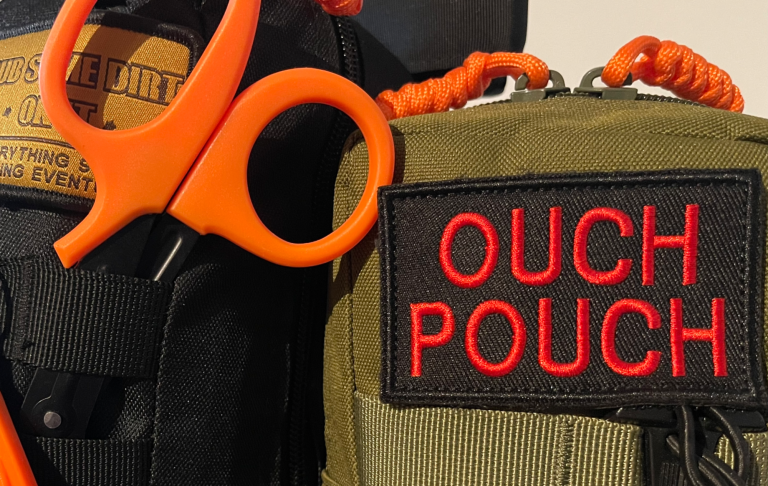 Orange sax och "OUCH POUCH" med svart och röd text på en grön väska.