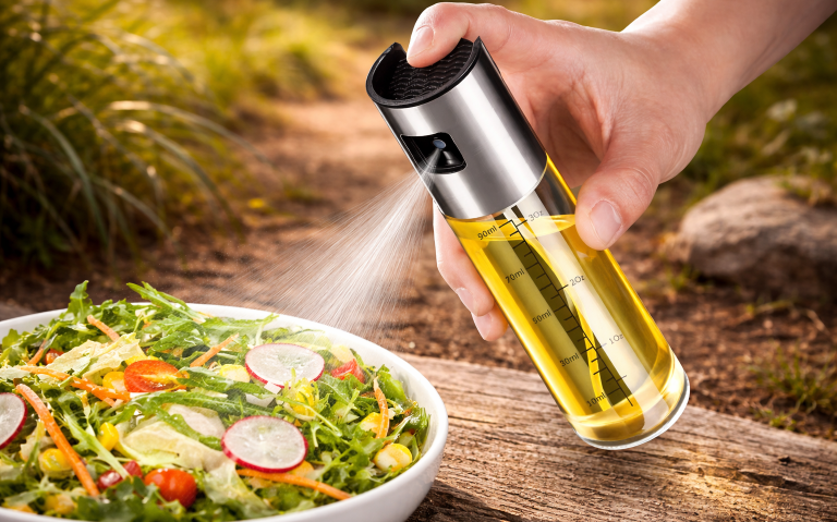 Hand sprayar olja över en fräsch sallad i naturmiljö.