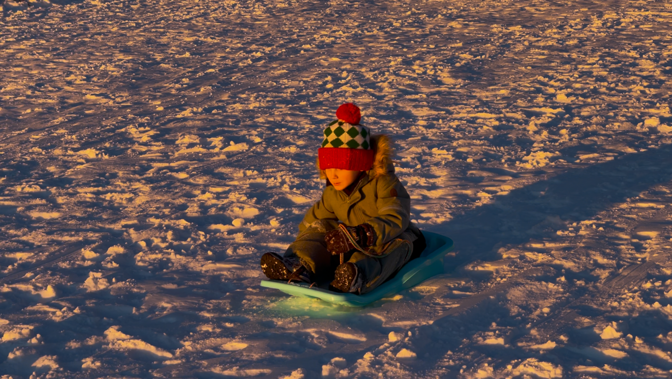 Pulka åkning Tjolöholm Barn åker kälke i snön, klädd i grön jacka och randig mössa, i solnedgångens ljus.