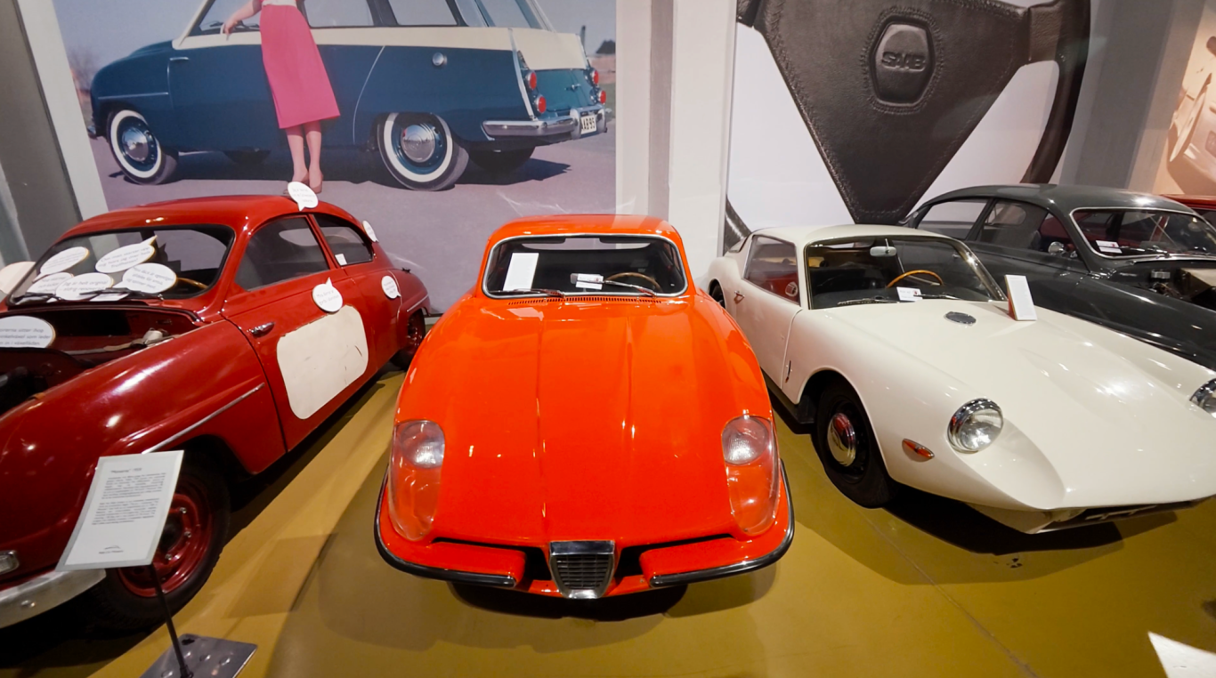 Saab Sonnet Tre klassiska sportbilar i en utställning, inklusive en röd bil i förgrunden.