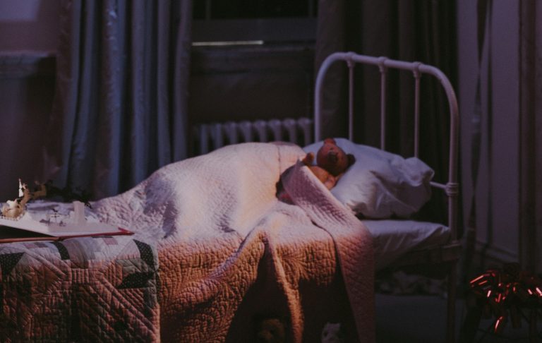 En person sover i en säng med filtar i ett dämpat rum.