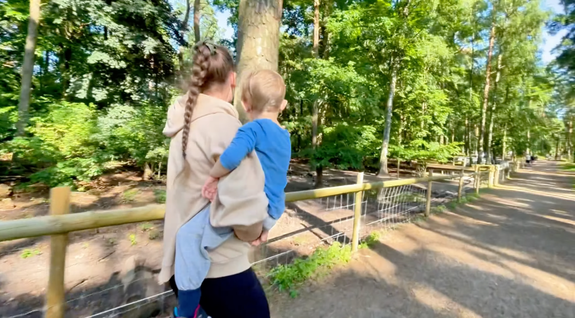 Grisar vid Vallarnas Friluftsområde Kvinna bär ett barn i skogen, omgiven av träd och grönska på en stig.