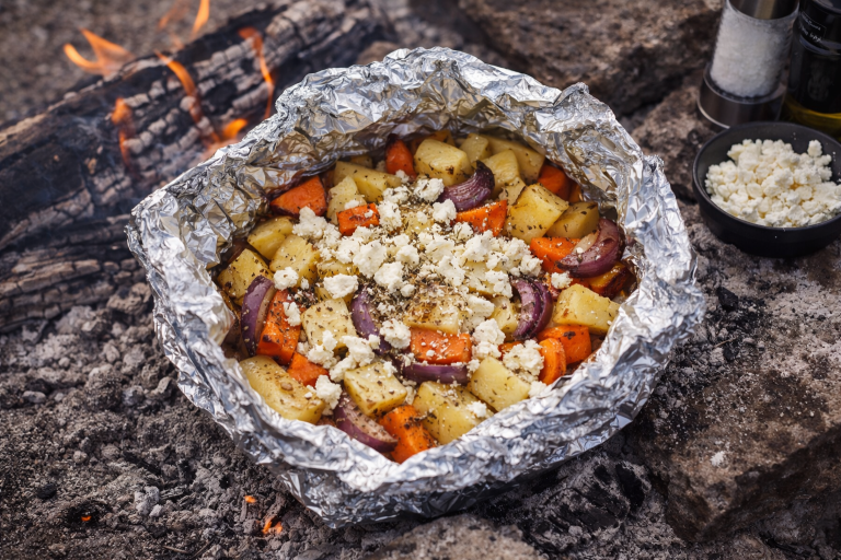 Grillpaket med potatis, morötter och kryddor på en eldplats.