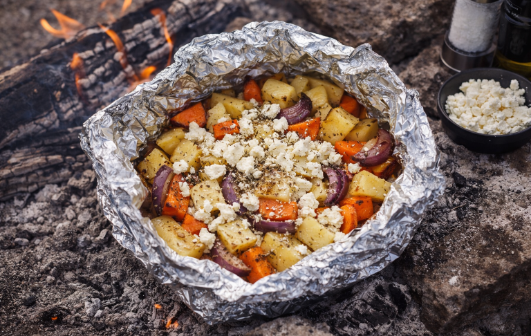Grillad potatis och grönsaker med ost, insvept i folie på en glödande grill.