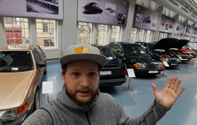 Johannes Framför massa Saab bilar Man med keps står i en bilutställning med flera klassiska bilar i bakgrunden.