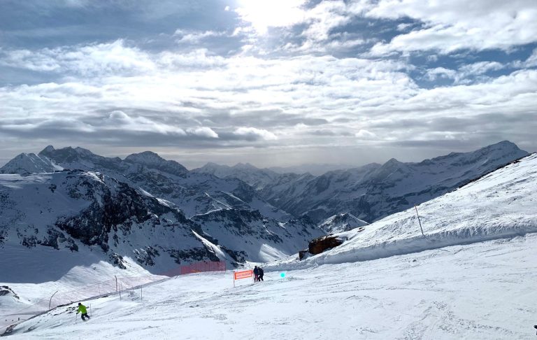 Snötäckta fjäll med skidåkare i fjärran under en molnig himmel.
