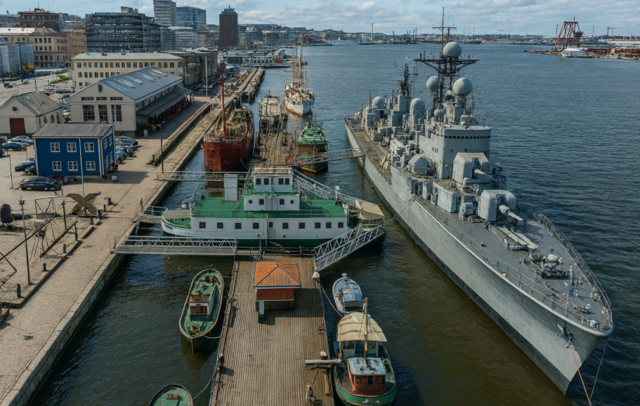 Illustration av Hamnmiljö med fartyg, kajer och byggnader vid vattnet.