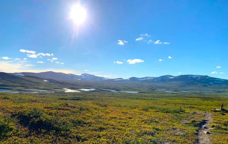 Landskap med fjäll, sjöar och en klarblå himmel under strålande sol.