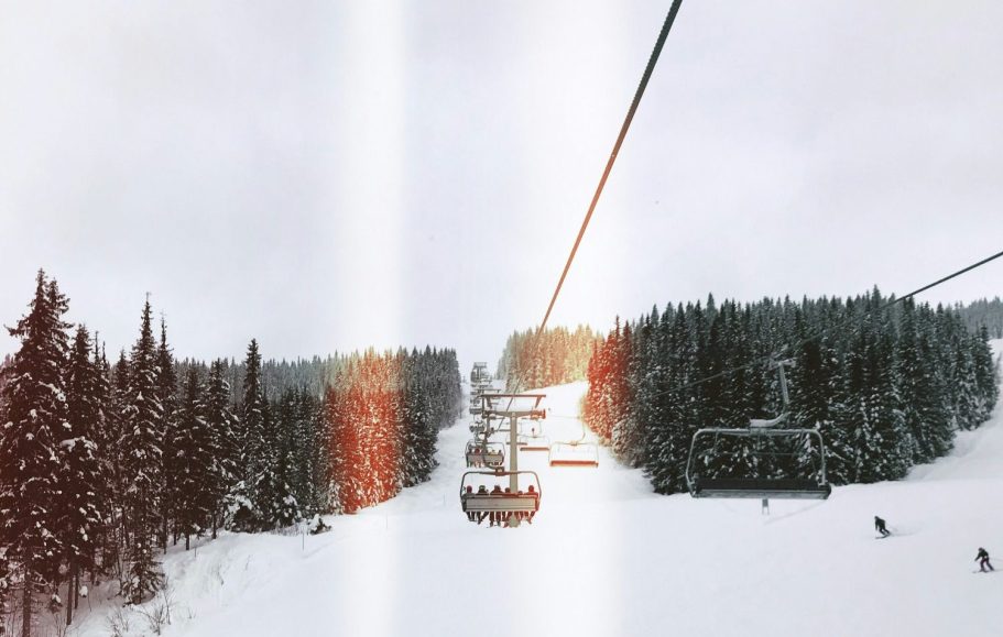 Person på skidlift med snöklädda berg i bakgrunden, grå himmel.
