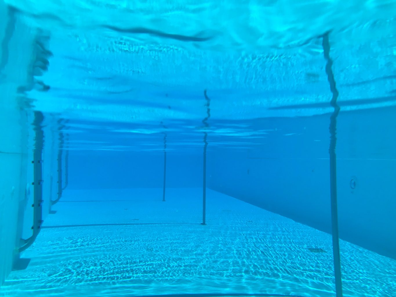 Poolen i vattnet Blått vatten i en simhall med vertikala linjer och en strålkastare i bakgrunden.