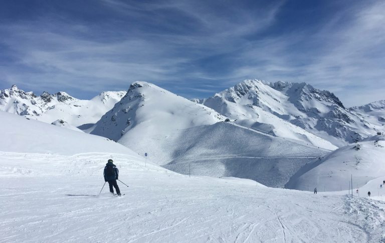 Skidåkare på snötäckta alpfjäll med blå himmel och vita moln.