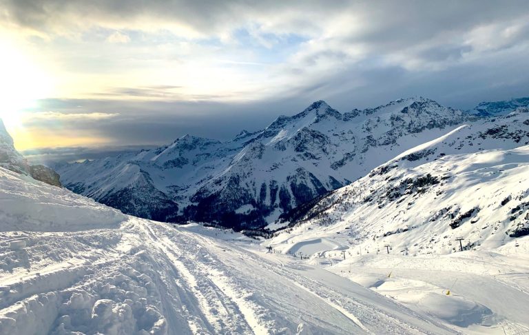 Vinterlandskap med snöklädda Alptoppar och en dimmig himmel i bakgrunden.