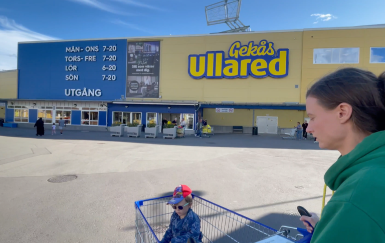 En kvinna står vid en köpcentrum som heter Ullared, med en barnvagn framför sig.