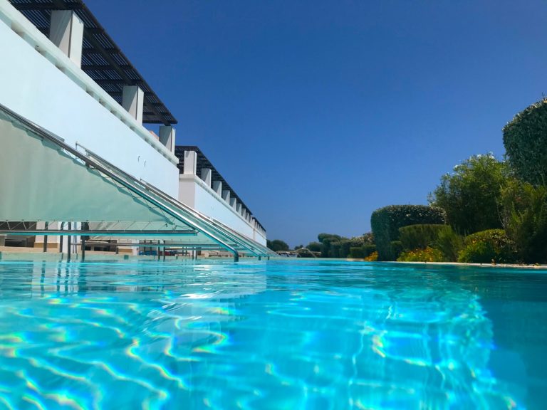 Klar blå pool med solbelysta kanter och omgivande grönska.