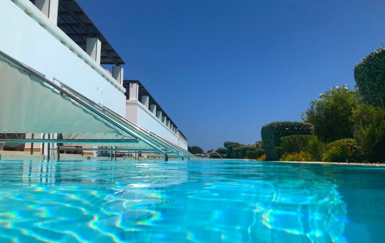 Kristallklart vatten i en swimmingpool med grönska i bakgrunden.