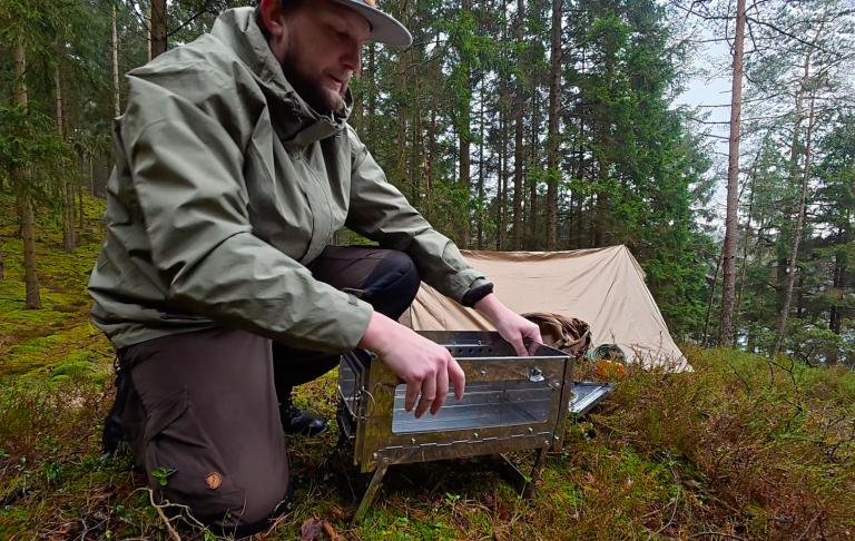 Man sätter upp en bärbar ugn nära ett tält i en skogsmiljö.