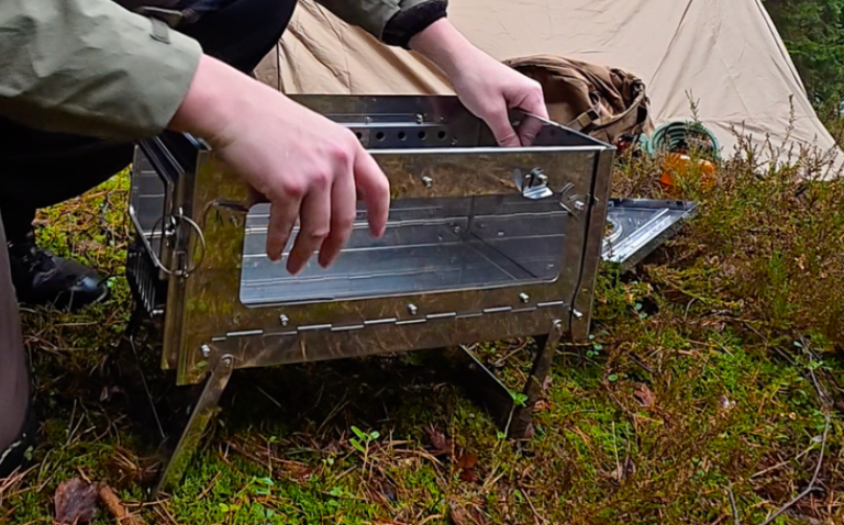 En person placerar en bärbar kamin på grön mossa nära ett tält.