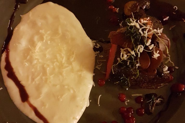 En tallrik med en portion mat som innehåller kött, grönsaker och en vit sås.