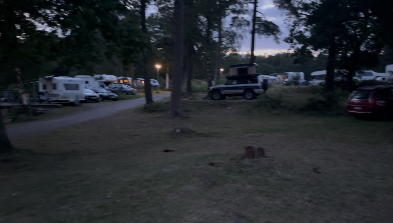 Campingtomterna Campingområde med flera husvagnar och bilar i skymning. Träd i förgrunden.