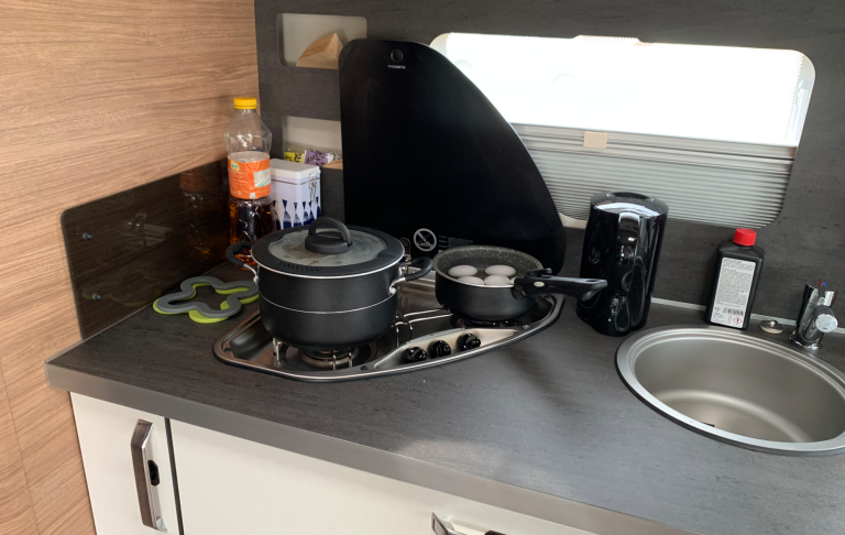 Kök med kokkärl, köksredskap och en diskho i en kompakt båt eller husvagn.