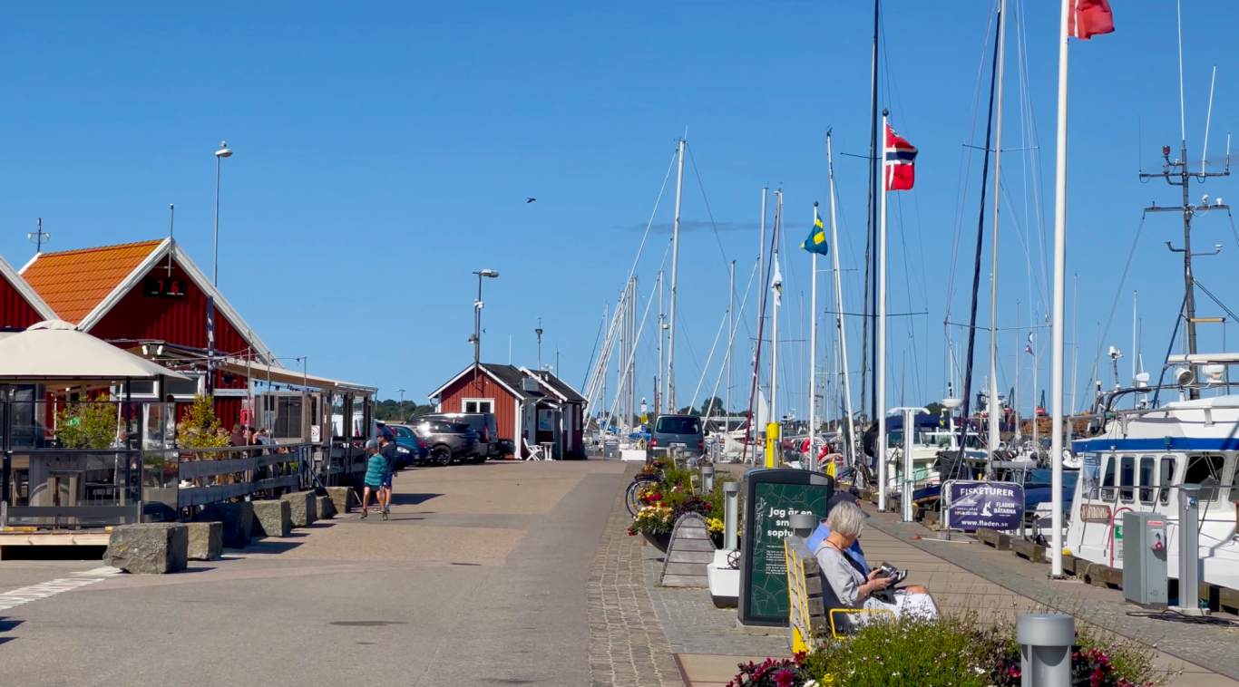 Hamnen vid Varbergs Fästning Hamnpromenad med segelbåtar och flaggor, omgiven av restauranger och hus.