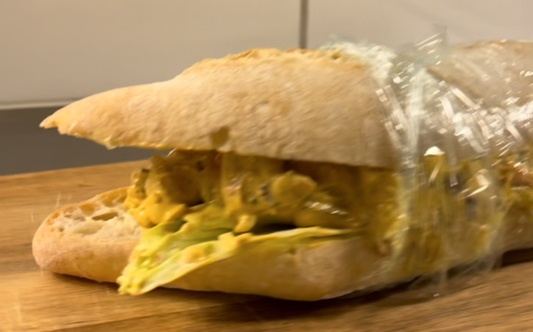 Smörgås med färgglad fyllning inslagen i plastfolie på en skärbräda.