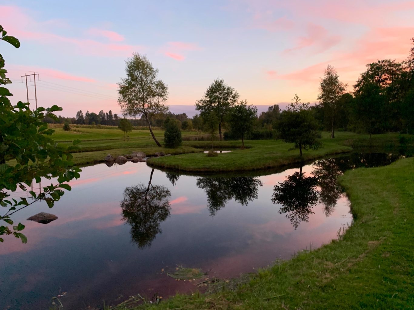Kvällssol i Flugströmmen hos Sunnedamm Lugn sjö med spegelbild av träd och en färgglad himmel vid skymning.