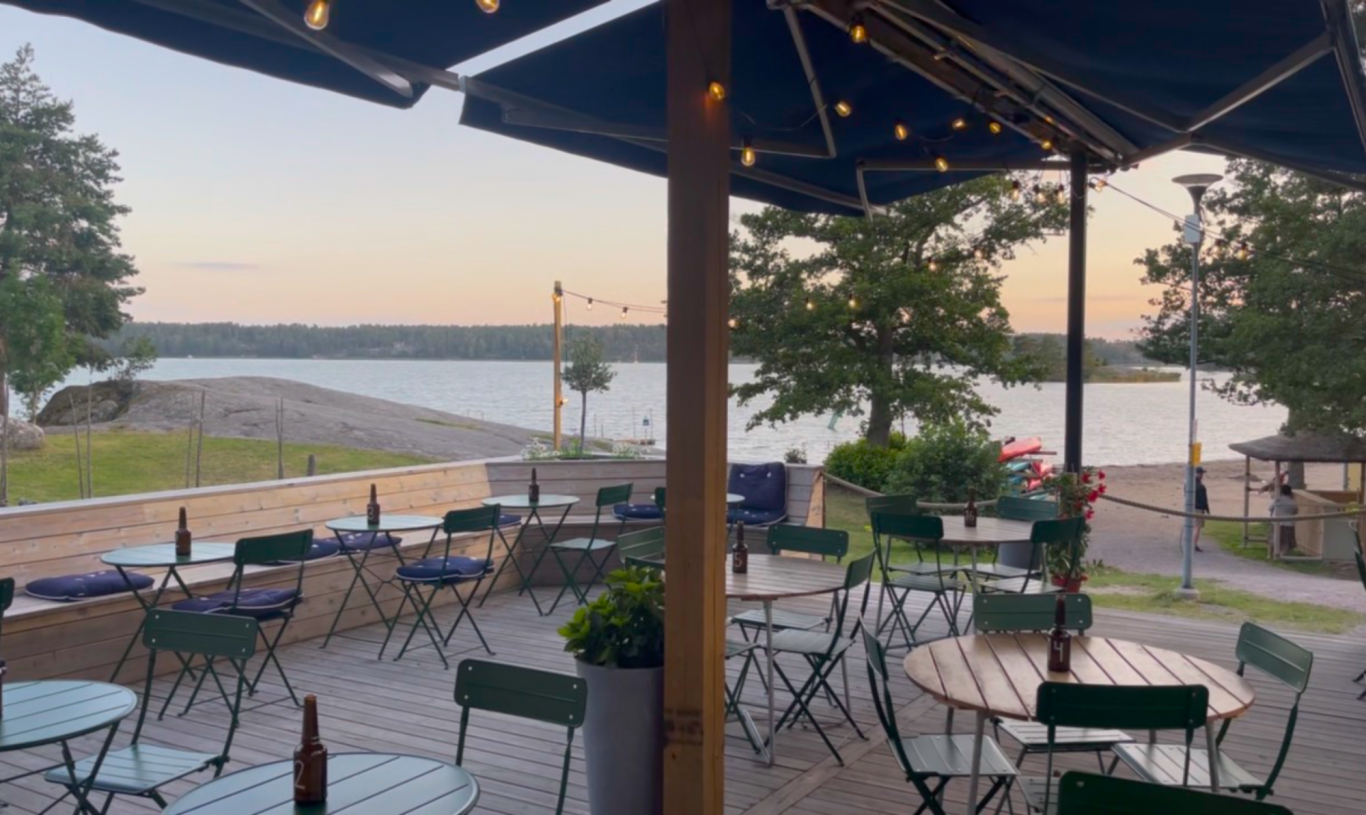 Algots på Udden Uteservering vid en sjö med bord, stolar och belysning i skymningen.