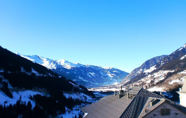 Snötäckta backar med träd och blå himmel med vita moln.