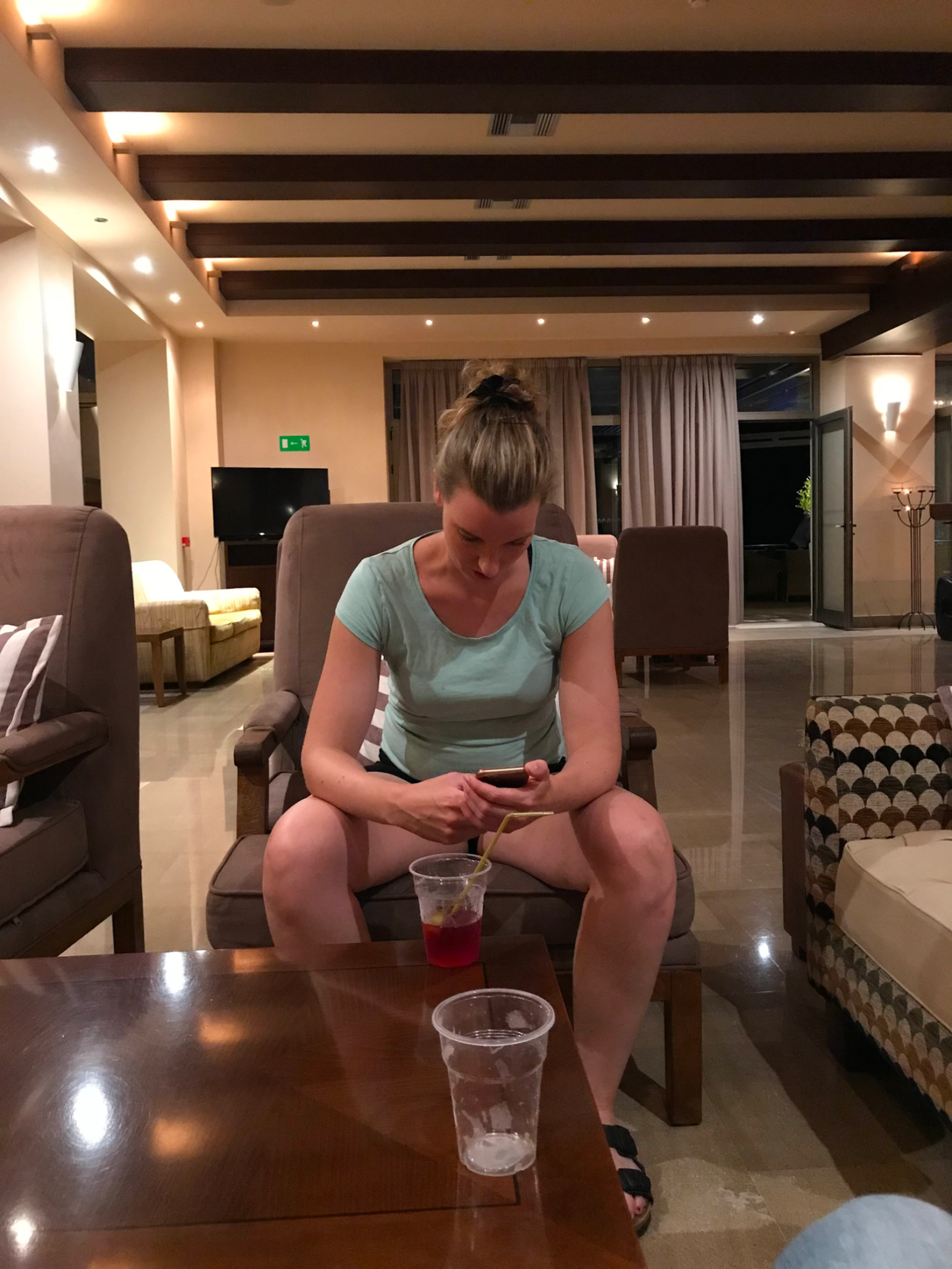 Kvälls Fördriv Kvinna sitter i en lounge och använder en mobiltelefon. Glass med is står bredvid.