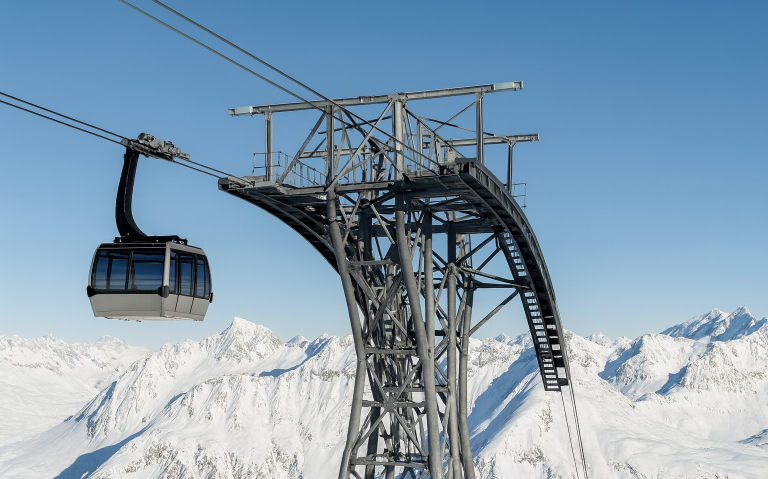 Stollift med gondol som svävar över snötäckta fjäll.