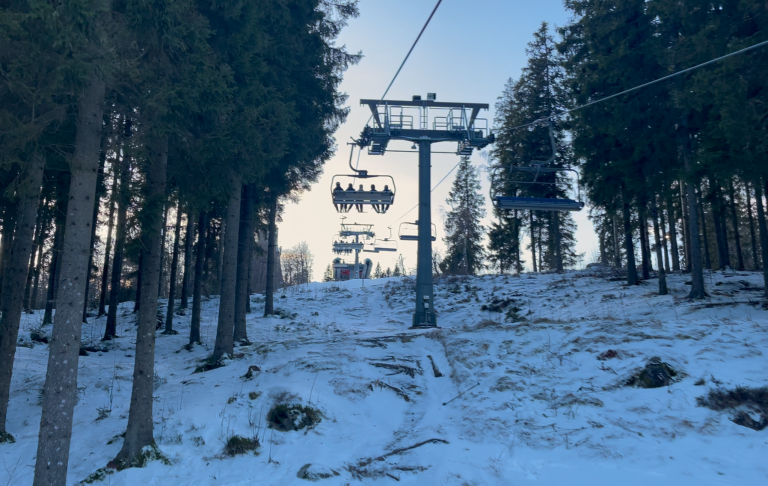 Skidbacke med stolslift mellan snötäckta träd på en klar dag.