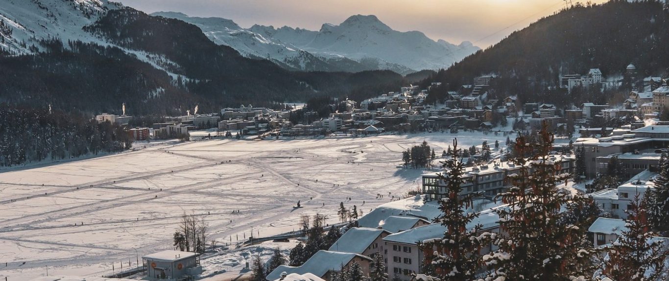 Vinterlandskap med snöklädda berg och en dal, belyst av en mjuk soluppgång.