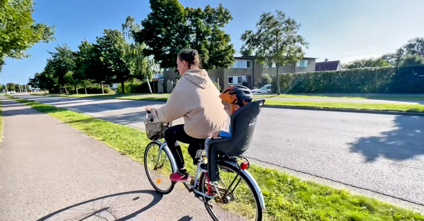 Cyklar till Vallarnas Friluftsområde En person cyklar på en väg med en ryggsäck och en säkerhetsväst.