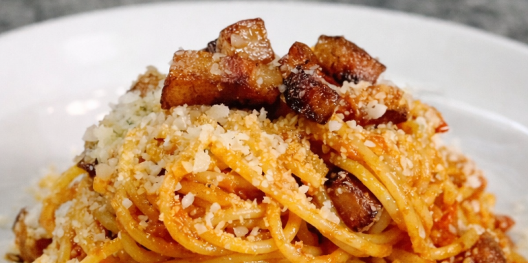 Tallrik med spaghetti toppad med bacon och riven ost.