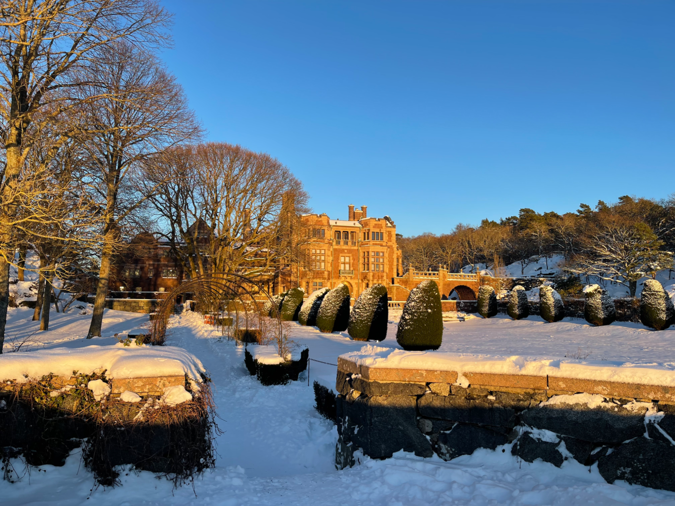 Tjolöholms Slott i Solnedgång Vinterlandskap med snöklädd mark, träd och en historia byggnad i bakgrunden.
