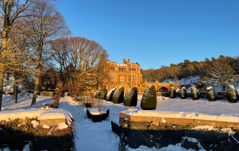 Vinterlandskap med ett gammalt hus, snöklädda träd och en stilla kanal.